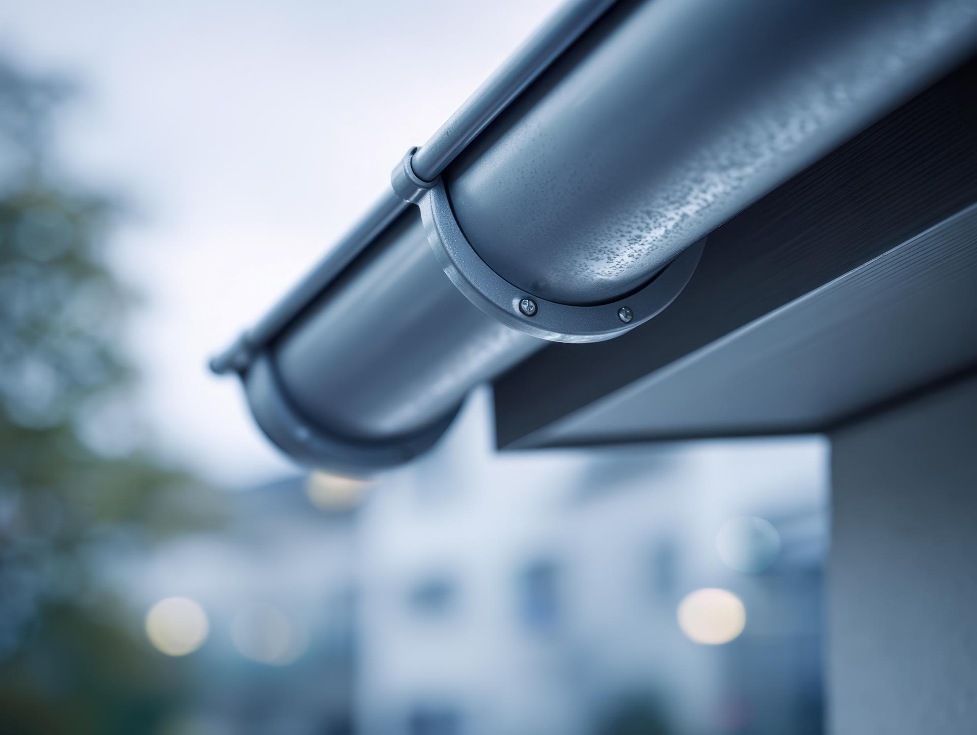 Close-up of a modern metal rain gutter system attached to a building roof edge with soft background bokeh effect on an overcast day